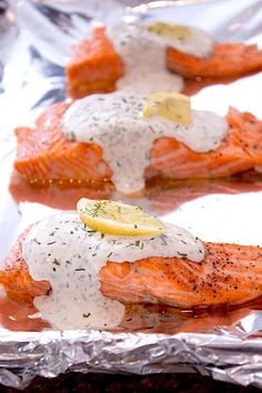 three salmon fillets with lemon and dill on top, sitting on tin foil