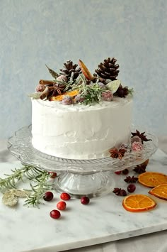 a white frosted cake sitting on top of a glass plate next to orange slices