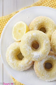 powdered sugar covered donuts on a white plate with lemon wedges next to them