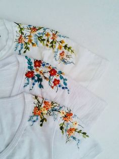 three white t - shirts with colorful flowers on them are laying next to each other