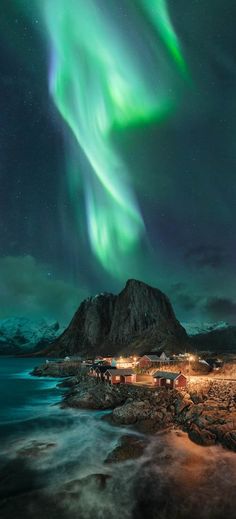 the northern lights shine brightly over houses and mountains in this landscape photo taken at night