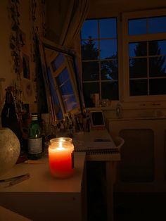 a lit candle sitting on top of a desk next to a window