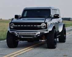 the front end of a silver truck driving down a road with grass in the background