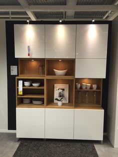 a white cabinet with bowls and plates on it in a room that has black walls