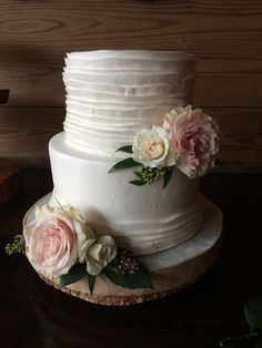 a three tiered white cake with pink flowers on the side and greenery around it