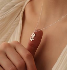 a woman wearing a white shirt holding a silver necklace with three flowers on the front