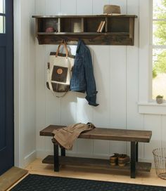 a wooden bench sitting under a window next to a coat rack and hat on top of it