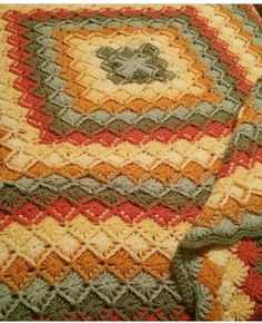 a crocheted blanket is laying on top of a wooden table with an orange, yellow and green afghan