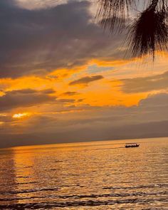 a boat floating on top of a large body of water under a cloudy sky at sunset