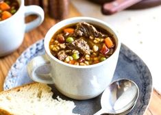 a bowl of soup on a plate next to a spoon and some slices of bread