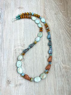 a necklace with beads and stones on a wooden surface, the bead is multicolored