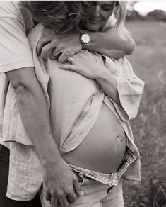 a pregnant woman hugging her husband in the grass