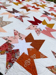 an orange and white quilt with many different colored stars on the top is laying on a table