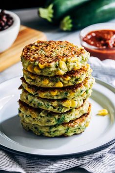 a stack of zucchini fritters on a white plate next to some chili sauce