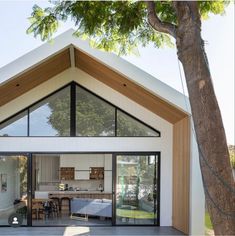 a modern house with large glass doors and wooden accents on the roof, surrounded by trees