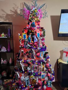 a brightly colored christmas tree decorated with barbies and other toys is shown in front of a flat screen tv