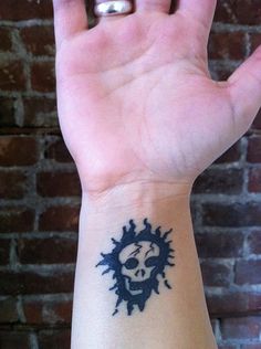 a person's hand with a skull and sun tattoo on the left side of their wrist