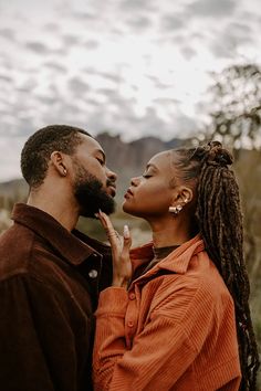 a man and woman standing close to each other in front of the sky with clouds