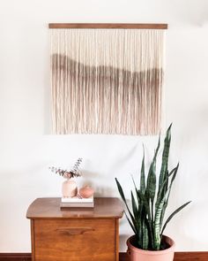 a wooden table topped with a potted plant next to a wall hanging