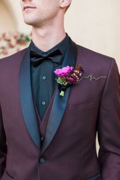 a man wearing a purple suit and black bow tie with a flower in his lapel