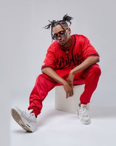 a man sitting on top of a white box wearing red sweatpants and sneakers with his hands in his pockets