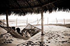 two people laying in a hammock on the beach