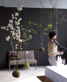 a woman standing in front of a table with flowers and vases hanging from it