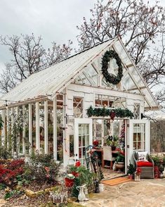 a white greenhouse with lots of potted plants and wreaths on the front door