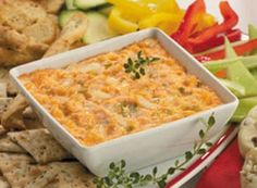 a bowl of dip surrounded by crackers and vegetables