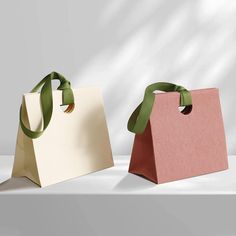 two paper bags with green ribbons on them sitting side by side in front of a white background