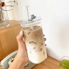 a person holding up a drink in front of a cup on a wooden counter top