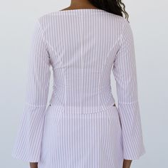 Handcrafted from Japanese lightweight pinstripe cotton poplin, the Lea Square Neck Flared Sleeve Top in Pinstripe Cotton features a square neckline with a subtle heart shape, flared long sleeves, fabric buttons trailing down the front, and pleats at the waist that create a narrow waistline and flared hem. The hem is designed to be shorter at the front and longer in the back. Pair it with the Cher Mini Skirt for a touch of 70s nostalgic charm, or dress it down with your favorite jeans for a casual outing.     Details & Care  Self-covered fabric buttons and loop closure at front  Unlined  100% Cotton Hand wash cold Dry clean recommend 100% Cotton Hand wash cold Chic Fitted Top With Vertical Stripes, Chic Fitted Vertical Stripes Tops, Chic Fitted Tops With Vertical Stripes, Fitted Pinstripe Tops For Summer, Fitted Pinstripe Summer Tops, Fitted Blouse With Vertical Stripes For Spring, Fitted Striped Blouse For Summer, Striped Fitted Blouse For Daywear, Fitted Striped Blouse For Daywear