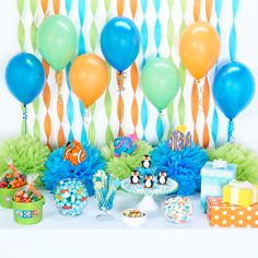 an assortment of balloons and decorations on a table with blue, green, orange, and white streamers