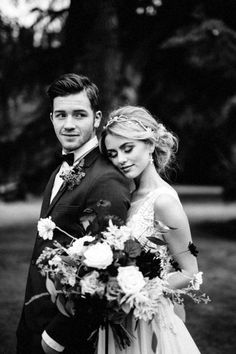 a man and woman standing next to each other in front of some trees with flowers