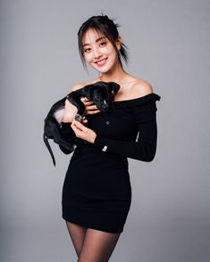 a woman holding a small black dog in her right hand and posing for the camera