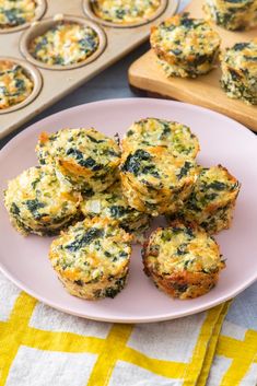 several muffins on a plate next to a tray of muffins with cheese and spinach