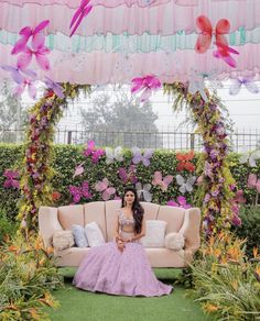 a woman sitting on top of a couch in front of a lush green field filled with flowers