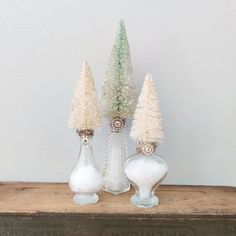 three glass vases sitting on top of a wooden table next to each other with small trees in them