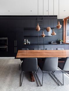 the modern kitchen has black cabinets and wooden table with grey chairs, along with hanging lights that hang from the ceiling