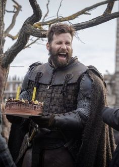 a man in armor holding a cake with candles on it while standing next to other men