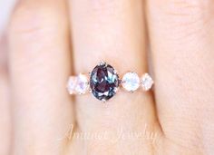 a woman's hand holding a ring with an oval blue and white diamond in it