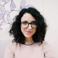 a woman with glasses is sitting in front of a flowered wall and smiling at the camera