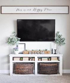 a tv mounted above a white table with baskets underneath it and a sign that says happy place