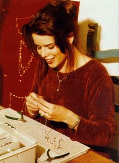 a woman sitting at a table with scissors in her hands and jewelry on the table