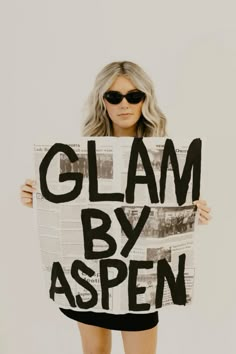 a woman holding up a sign that says glam by aspenn on it