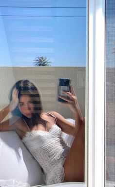 a woman in a white dress is taking a selfie through a window with her cell phone