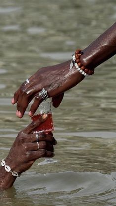 two hands reaching out to each other in the water with bracelets on their wrists