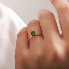 a woman's hand holding a ring with a green gemstone on the middle