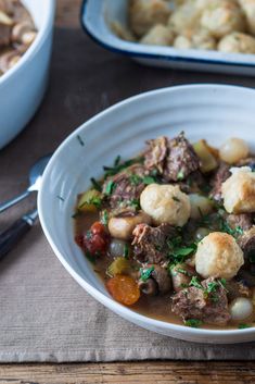 a white bowl filled with meat and dumplings on top of a table next to another bowl