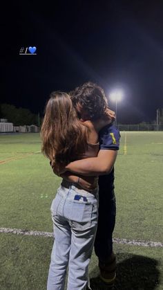 two children hugging each other on a soccer field at night with lights in the background